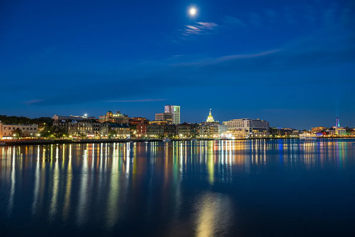 Savannah riverfront skyline reflected on the water beneath a full moon